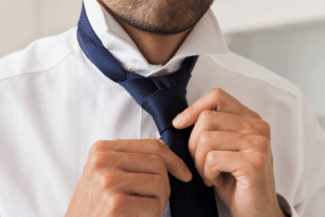 Mains nouant une cravate bleu marine sur une chemise blanche